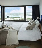 Doppelbett mit naturfarbenen Bezügen in Schlafzimmer mit Landschaftsblick durch Übereck-Panoramafenster