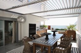 Rattan chairs around wooden table on terrace with slatted roof