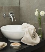 Wall-mounted tap above washstand with countertop basin; draped towel and flower arrangement