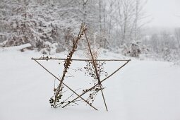 Star made from twigs decorated with dried flowers and larch cones in snowy landscape