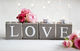 Rosarote Rosenblüten und Teelichter auf Pappwürfeln mit Typoprint 'LOVE'