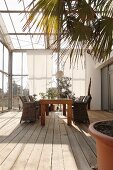 Dining area in conservatory with rustic wooden floor and floor-length sunshade curtains on glass façade