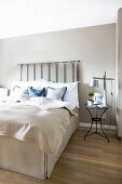 Box-spring bed with pale valance and bedspread and upholstered headboard hung on wall painted pale grey in elegant bedroom