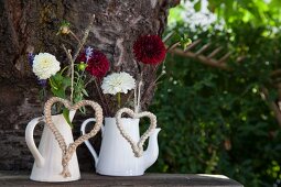 Gartnblumen mit Makramee-Herzen in weissen Vintage-Kannen