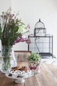 Planter, bouquet and cake stands on dining table in front of vintage-style birdcage