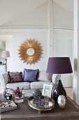 Purple table lamp on coffee table, sofa and sunburst mirror on wall