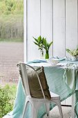 Pastel tablecloth, vases of lily of the valley and place settings on table next to chair with cushion