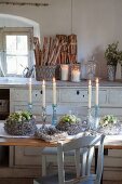 Wreath of cream polyantha roses and candlesticks on rustic table in country-style kitchen