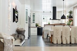 Loose-covered chairs with lacing in dining area of open-plan kitchen with black extractor hood above counter