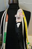 Schwarze Schneiderpuppe mit umgehängten Massbändern und Puppe