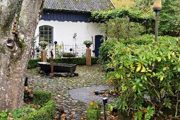 Vintage zinc bathtub on pebble-cobbled terrace in garden of white-painted country house