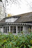 Blick vom Garten auf Wohnhaus mit Anbau, an Fenster und Traufkante befestigtes Zierbrett grau lackiert