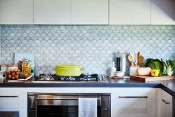 White kitchen with L-shaped counter, gas hob and splashback with fish-scale pattern