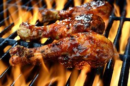 Three chicken legs in BBQ sauce cooking on a flaming grill