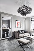 Upholstered stool and sofa around coffee table below chandelier hanging from stucco ceiling in elegant living room