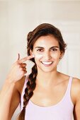 Young, brunette woman with braided hair applying cream to face