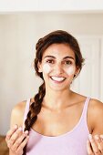 Young, brunette woman with braided hair applying cream to face