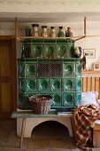 Traditional tiled stove, bench and wicker basket in restored farmhouse