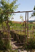 Gartentor aus naturbelassenen Holzstäben und Blick in sommerliche Landschaft