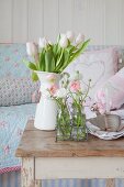 Spring arrangement of tulips and ranunculus in enamel jug and glass bottles on old table