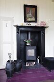 Fireplace accessories on purple-painted wooden floor next to cast iron stove in old fireplace