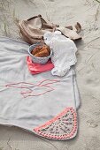 Pale grey picnic blanket with crocheted trim and seagull motif on sand