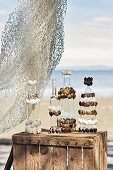 Glasflaschen dekoriert mit Muscheln auf Holzkiste am Strand