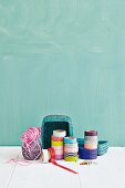 Rolls of washi tape, reels of thread and basket against turquoise wall