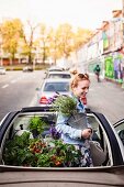 Urban gardening: young woman in convertible car with foliage plants and vegetable plants