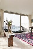 Branches in glass vase on rustic wooden bench, metal chair next to table and glass wall with view of harbour entrance