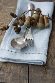 Silver spoons on linen napkin held in ring threaded with acorns