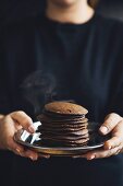 A woman holding a stack of orange and cocoa pancakes