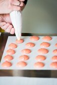 Pink macaroons being piped onto baking paper