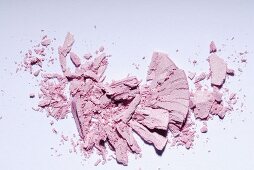 Rose-coloured eye shadow crumbled on a white surface