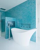 Expressiv geformte Designerbadewanne und Standarmatur in elegantem Bad mit blau schimmernden Mosaikfliesen