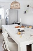 White-painted, solid wooden table below wicker lampshade in kitchen-dining room