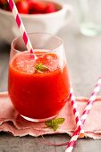 A strawberry and watermelon smoothie in a glass with a straw