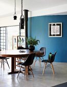 Classic shell chairs around oval wooden table in front of curved blue wall
