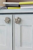 Möbelgriffe in Blütenform aus Beton an Türen eines hellgrau getönten Schränkchens