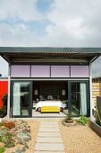 View from roof terrace along stepping-stone path leading through gravel to open glass sliding doors and into bedroom of shipping container house