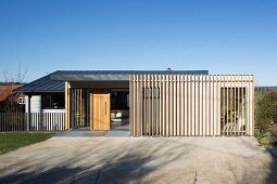 Blue sky above contemporary house; wooden front door, glass walls and wooden structure in front of facade