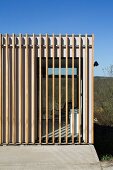 Detail of facade of contemporary house with vertical wooden structure providing shading; view into interior through glass wall