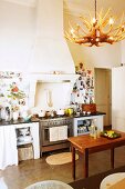 Wooden table in front of kitchen counter with gas cooker below masonry mantel hood in traditional kitchen with lampshade made from antlers and decorated walls