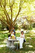 Family in sunny, summery garden around set table under shady tree