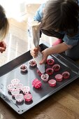 Kind füllt Teigmasse für Mini-Schokoladenmuffins in Papierförmchen