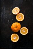 Seville oranges, whole and halved on a black surface