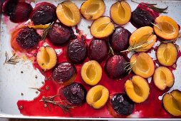 Oven roasted damsons with rosemary on a baking tray (seen from above)