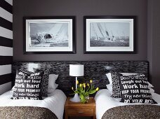 Black and white scatter cushions with lettering on covers on twin beds below photos of sailing boats on dark wall