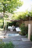 Terrace with wooden floor, outdoor shower and woman sitting in comfortable seating area below pergola