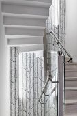Stairwell with stainless steel handrail on glass balustrade and tree-patterned mural wallpaper in background